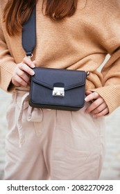 Closeup of black small handbag in woman's hand. Fall spring fashion outfit camel sweater and trendy white jeans. Fashion detail, stylish small bag.  