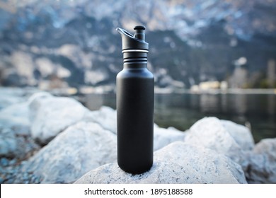 Close-up black of steel eco thermo water bottle on the background of the lake in the mountains. Copy space. Zero waste, no plastic, sustainability.