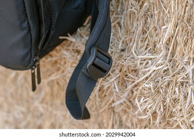 A close-up of the black strap of the backpack against the yellow hay. Black plastic buckle that adjusts the length of the backpack strap. Selective focus. Defocus, blur, noise, grain effect
