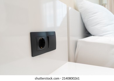 Close-up of a black switch and socket on a white wall near the bed