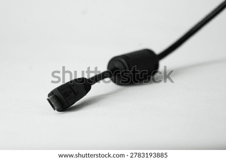 Close-up of a black USB data cable with ferrite core bead.

A high-angle close-up photograph of a black digital data transfer or charging cable connector lying diagonally on a clean white surface. The image highlights the cylindrical ferrite core bead attached to the wire, used for electronic noise reduction and interference suppression. Ideal for technical hardware documentation, electronics repair guides, and IT accessory product listings.