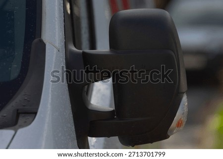 Closeup black van side mirror highlighting visibility and indicator, textured plastic housing with integrated signal, shallow depthoffield and blurred street background, commercial route context