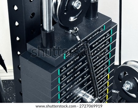 Close-up of a black weight stack on a cable machine in a modern fitness center with pound and kilogram markings.