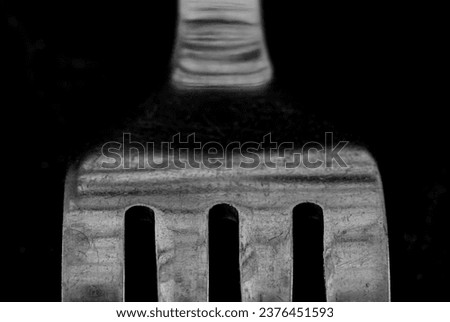 A close-up black and white photo of a fork on a black background. The fork is stainless steel and it has four tines. The tines are slightly curved and the handle is long and slender. 