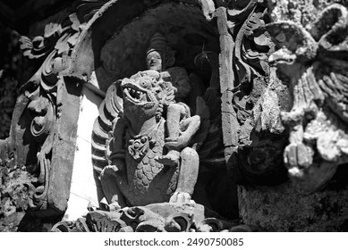 A close-up black and white photograph captures a statue resembling Vishnu riding Garuda at the Bali temple, nestled within a wall cavity resembling a small cave, half-illuminated by the sunrise. - Powered by Shutterstock