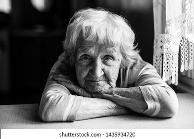 Close-up Black And White Portrait Of A Old Woman At The Table In Home.