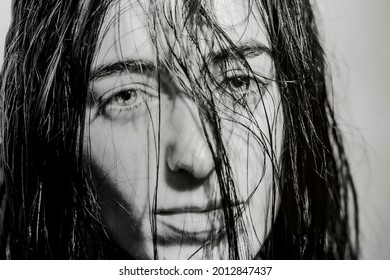 Close-up Black And White Portrait Of White Woman.  Her Gaze Is Observed Through Her Wet Hair. She Is Looking At The Camera, Not Smiling.