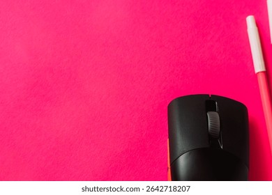 Close-up of a black wireless computer mouse and a pink pen on a vibrant hot pink background. Flat lay for creative workspace or tech concept.