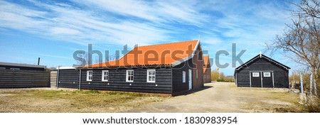 Close-up of a black wooden countryside house with a red tile roof in Zeeland, the Netherlands. Panoramic view of a small village. Construction industry, architecture, travel, tourism