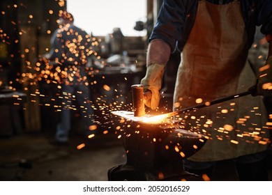 Close-up of blacksmith in apron working with hammer and iron in the workshop