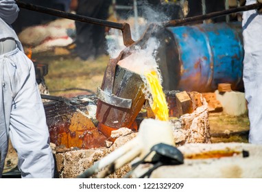 Close-up Of Blacksmith Holding A Hot Crucible By The Iron Pliers From Furnace And Pouring The Melting Gold Into The Statue Block. The Process To Making Of Metal Statue In Local Thailand Traditional.