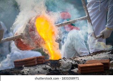 Close-up Of Blacksmith Holding A Hot Crucible By The Iron Pliers From Furnace And Pouring The Melting Gold Into The Statue Block. The Process To Making Of Metal Statue In Local Thailand Traditional.