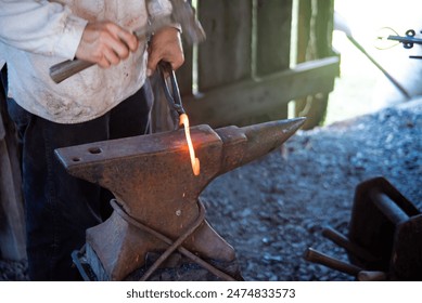 Close-up blacksmith man hand using long carbon steel tongs with steel rivets and hammer to forge cast iron horseshoes melting on medieval anvil at traditional trade workshop, Mansfield, Missouri. USA - Powered by Shutterstock