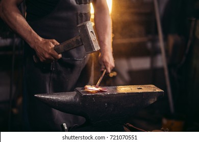 Close-up of blacksmith manually forging the molten metal on the anvil in smithy workshop. Blacksmith working metal with hammer in the forge