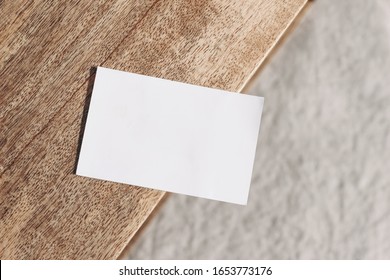 Closeup Of Blank Business Card On Teak Wooden Table. Blurred Beige Linen Background. Empty Paper Card Mockup Scene In Neutral Colors. Branding, Business Concept. Sparse Composition Top View.