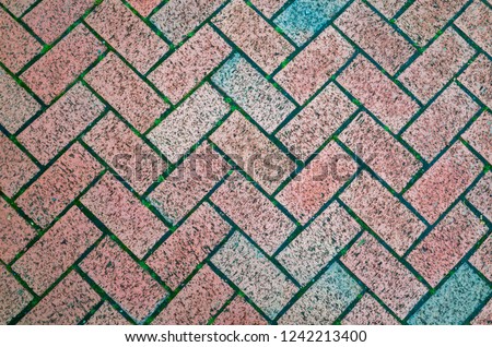 A close-up of block paving bricks set in a herringbone pattern with faded colours. Rustic textured background or flat lay concept.