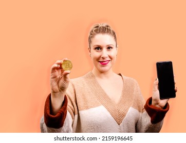 A Closeup Of A Blonde Woman Showing A Bitcoin Coin While Holding A Mobile Phone In A White Background