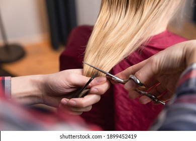 Closeup of blonde women willing to cut ponytail. Hairdresser with scissors at home starting to cut hair.