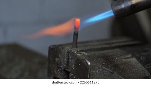 Close-up. A blowtorch heated a piece of metal rod. The metal burns bright red when heated by a blowtorch. A man soldering metal with a blowtorch. - Powered by Shutterstock