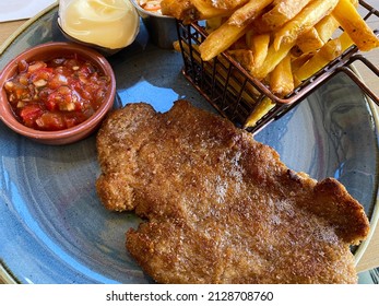 Closeup of blue dish with breaded escalope schnitzel, metal basket french fries and choise of sauces 