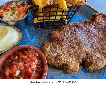 Closeup of blue dish with breaded escalope schnitzel, metal basket french fries and choise of sauces