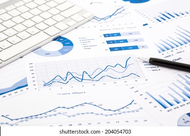 Closeup Blue Graph And Chart Reports With White Keyboard And Pen On Office Table, Financial And Business Concept