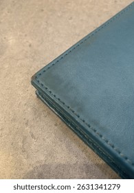 Close-up of a blue leather wallet corner with fine stitching—sleek, refined, and timeless. A perfect blend of craftsmanship and style on a soft, neutral backdrop.