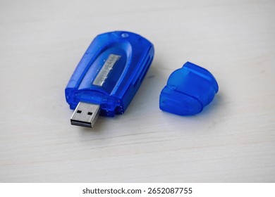 Close-up of a blue memory card reader resting on a light wooden surface. Its protective cap sits beside, ready for use. Ideal for technology, data, and digital storage concepts.