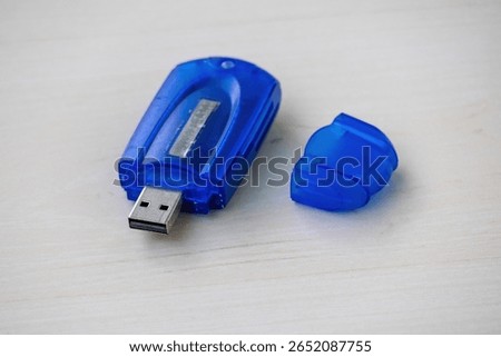 Close-up of a blue memory card reader resting on a light wooden surface. Its protective cap sits beside, ready for use. Ideal for technology, data, and digital storage concepts.