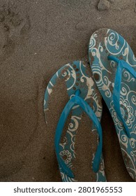 A close-up of blue patterned flip-flops resting on sandy beach, capturing a relaxed summer vibe.