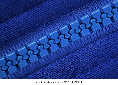 Close-up of a blue plastic zipper closed in the middle of a blue fabric texture