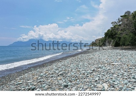 Close-up of blue stones on the beach of Pantai Batu Biru, the Blue Stone Beach, in the background a hill, in Ende on Flores.