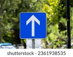 Close-up of blue and white one way road sign with arrow and car parking of castle at Slovenian City of Bled on a blue cloudy summer day. Photo taken August 8th, 2023, Bled, Slovenia.