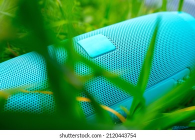 A Close-up Of A Blue Wireless Music Speaker Lying Among The Dense Green Grass. Modern Devices For Playing Music. Selective Focus