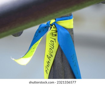 A closeup of a blue and yellow ribbon tied to a metal pole in support of Ukraine