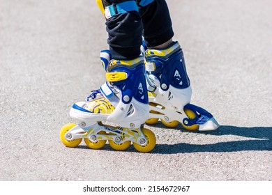 Close-up of blue yellow and wite children's roller skates. Cropped shot of a little child learning to rollerblade on the asphalt. Sunny summer day 