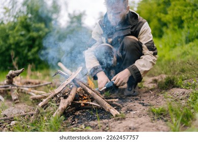 Close-up of blurred survivalist male in raincoat starting fire using gas lighter on bank of river for cooking and warming in evening before sunset. Concept of exploration, travel and adventure. - Powered by Shutterstock
