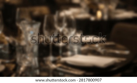A close-up, blurred view of a formal dining table set for a meal with wine glasses and cutlery, suggesting a fine dining experience.