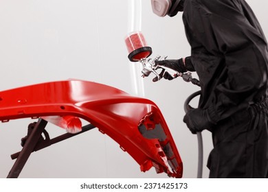 Close-up of a bodywork mechanic working in the workshop painting a car front bumper	
