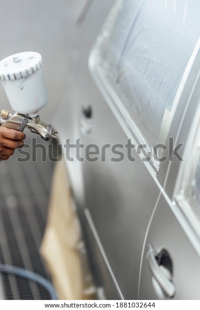 Close-up of a bodywork mechanic working in the\
workshop painting a\
car