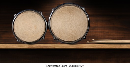 Close-up of bongo drums and a pair of drumsticks, above a wooden shelf with copy space. Percussion instrument. Photography.