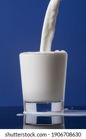Bouteille de lait en gros plan versant dans un verre au bord et isolée sur fond bleu