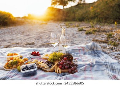 Close-up of bottle of wine and two glasses outdoors. Picnic on the beach. Delicious snacks, bread, fruits and berries on the bedspread. - Powered by Shutterstock