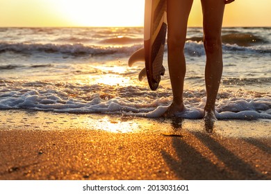 Close-up Bottom Pov View Young Adult Female Surfer Girl Legs With Surfboard Stand At Ocean Coast Wave Against Warm Sunrise Or Sunset Sun. Sport Healthy Carefree Freedom Lifestyle Vacation Concept