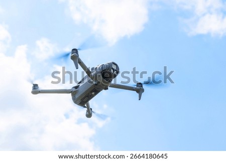 Close-up bottom view of flying drone with camera facing forward under blue sky