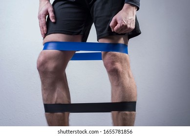 Closeup, Bottom View Of The Guys Muscular Legs In Sports Shorts, Stretching Fitness Elastic Bands With His Legs, Involvement Of Leg Muscle Groups That Are Not Involved In Everyday Life.