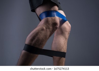 Closeup, Bottom View Of The Guys Muscular Legs In Sports Shorts, Stretching Fitness Elastic Bands With His Legs, Involvement Of Leg Muscle Groups That Are Not Involved In Everyday Life.