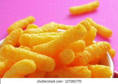 Closeup Of A Bowl With Cheese Puffs On A Pink Background