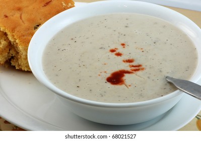 Closeup Of Bowl Of Cream Of Mushroom Soup On White Plate With Dab Of Louisiana Hot Sauce And Slab Of Cornbread.