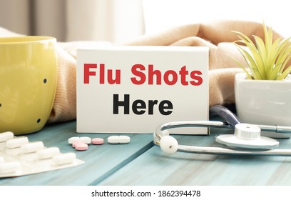 A Close-up Of A Box That Reads Flu Shots Here. Pills, Mug And Stethoscope On The Background.